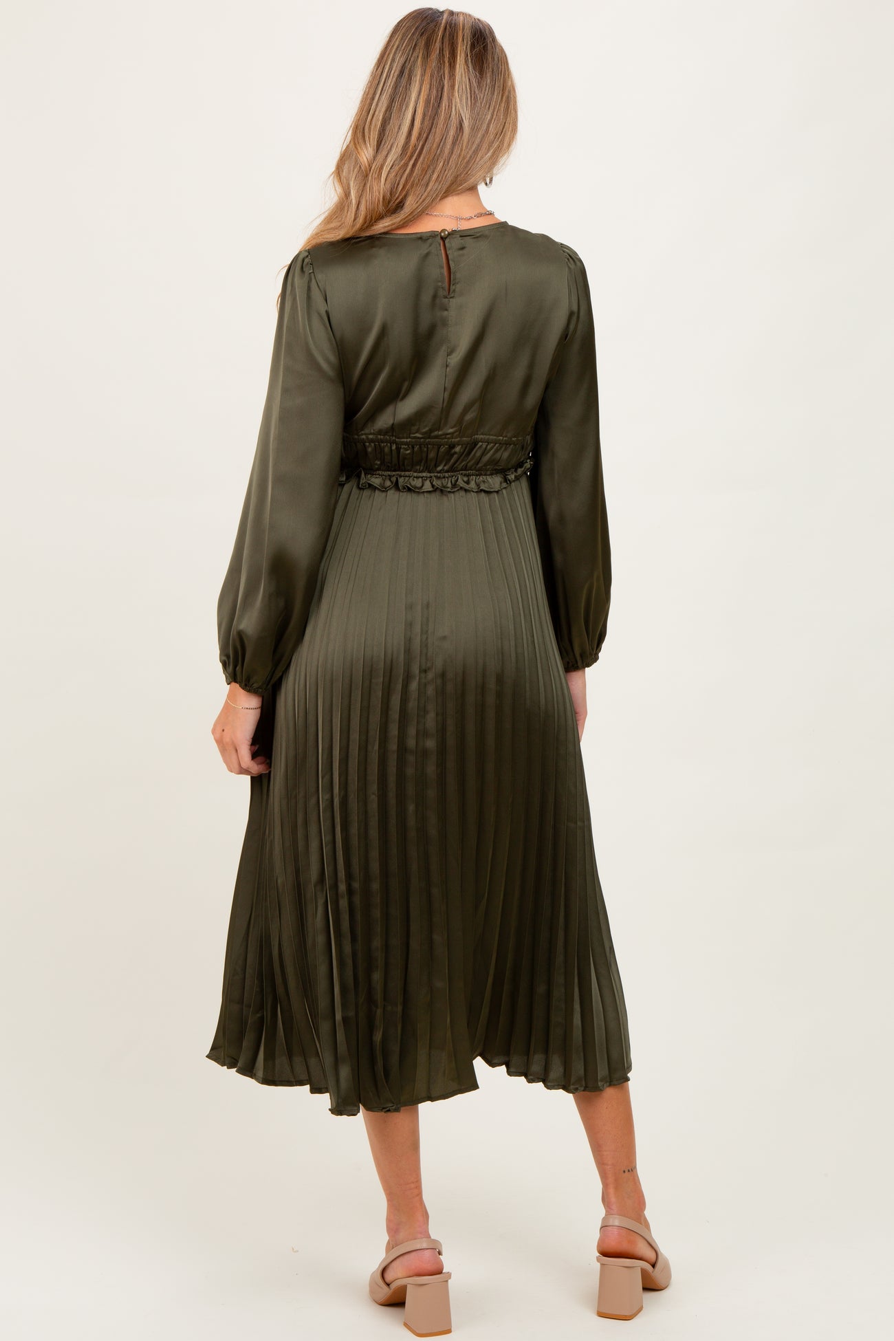 woman wearing a dark green pleated maternity dress with long sleeves and a cinched waist, showing the back view