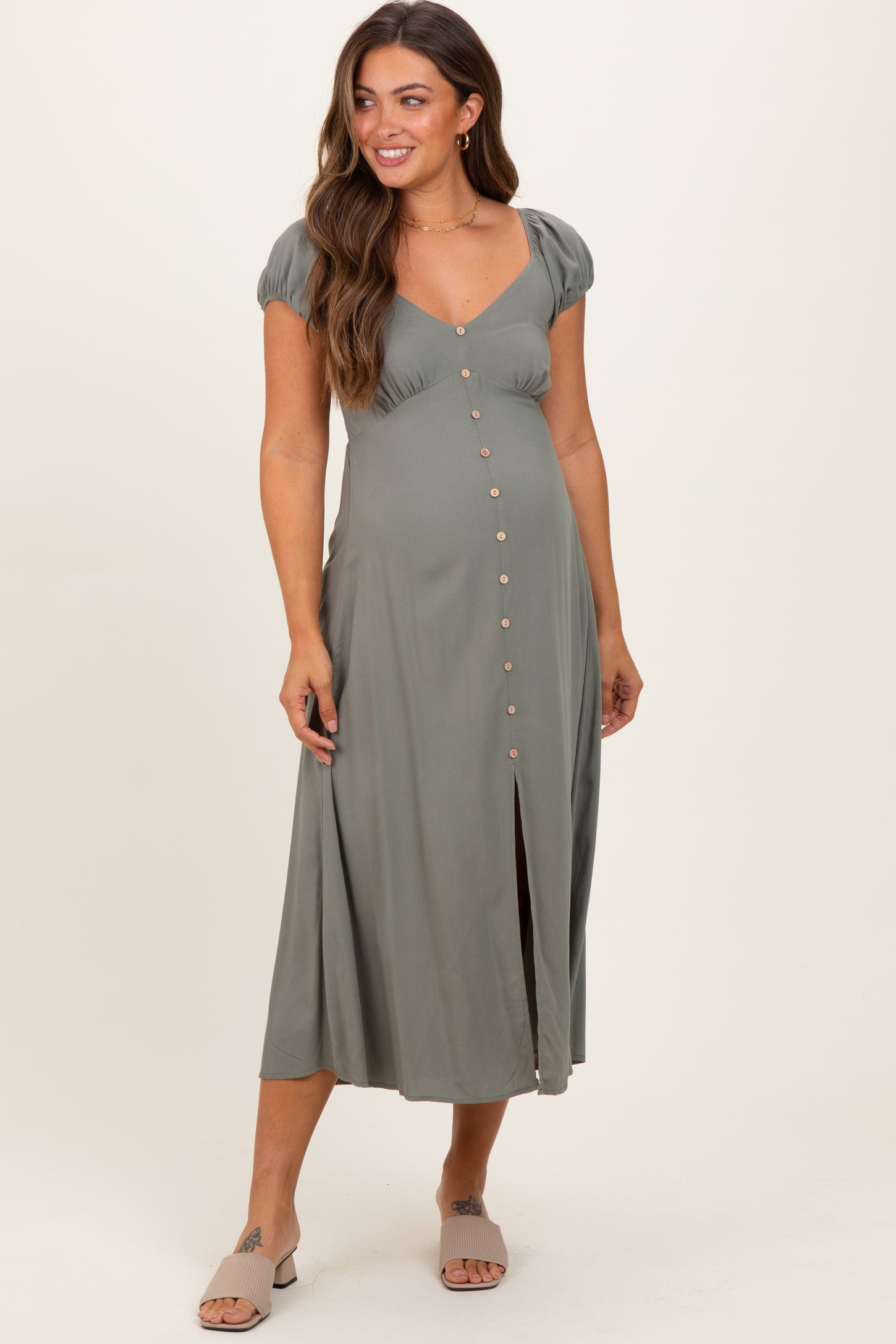 woman wearing a dusty green maternity maxi dress with puff sleeves and button detail, showcasing a visible baby bump