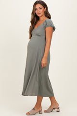 woman wearing a sage green maternity dress with short puff sleeves and button details, showing her baby bump