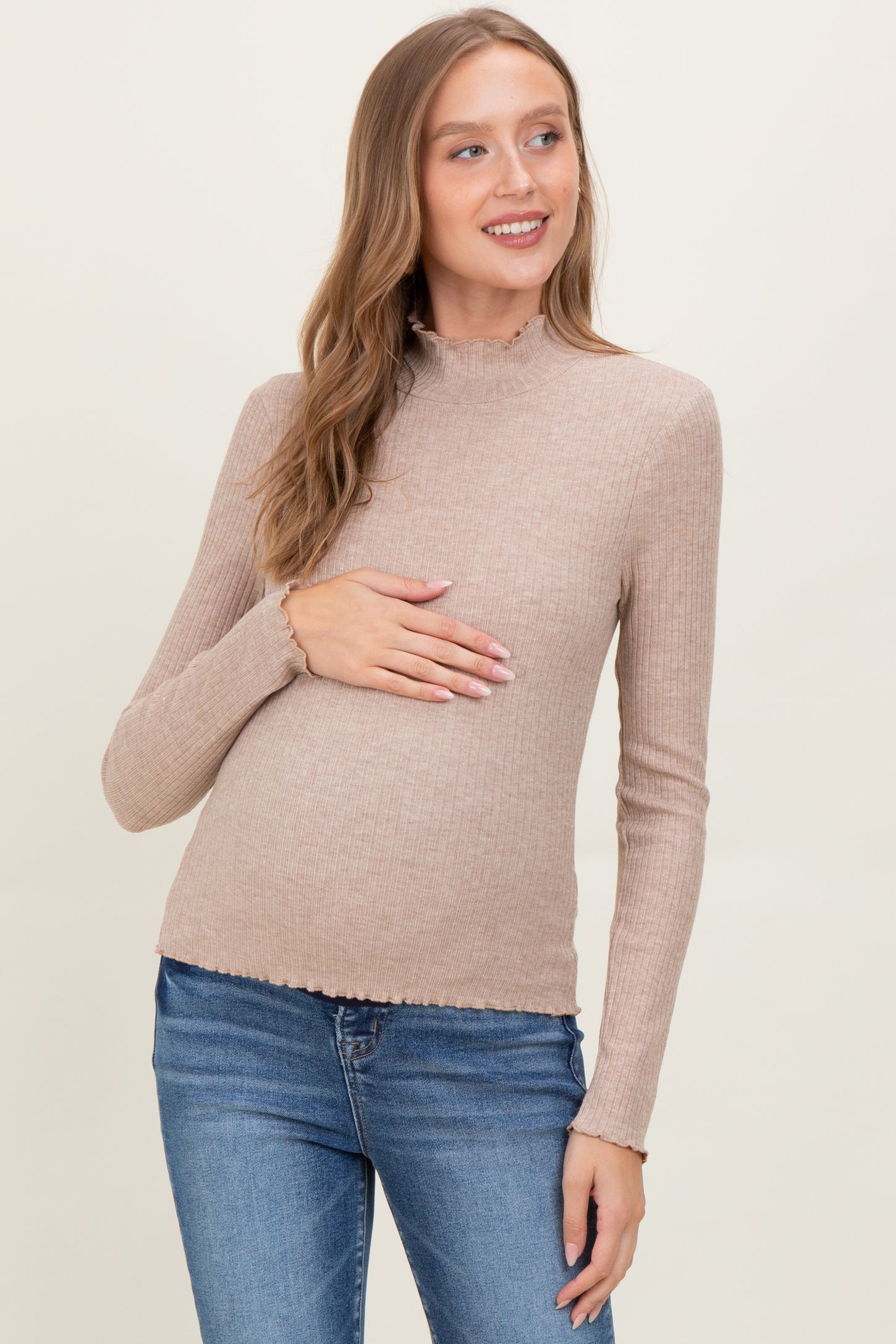 woman wearing a beige long sleeve maternity top with a scalloped hem, holding her baby bump