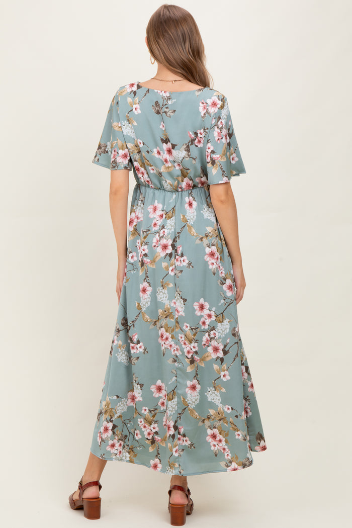 woman wearing a floral patterned maternity maxi dress in light blue with short sleeves and a cinched waist, showing a baby bump