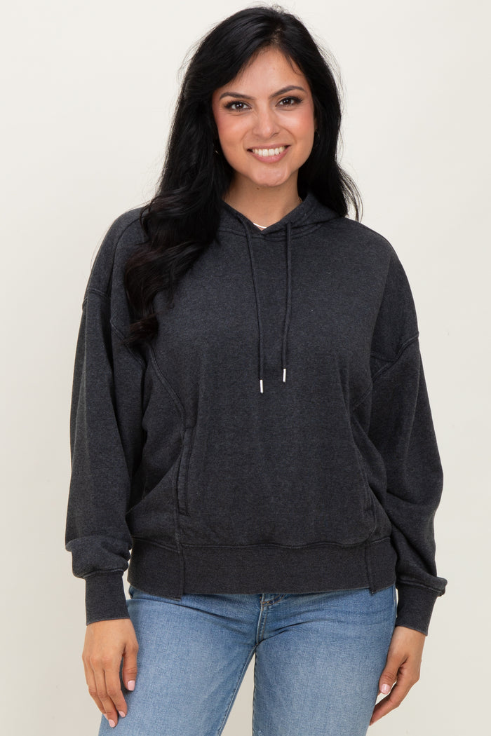 woman wearing a dark gray oversized hoodie with a front pocket and drawstrings, smiling at the camera