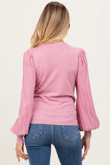 woman wearing a light pink maternity top with puffed sleeves and ribbed detailing, featuring a fitted silhouette