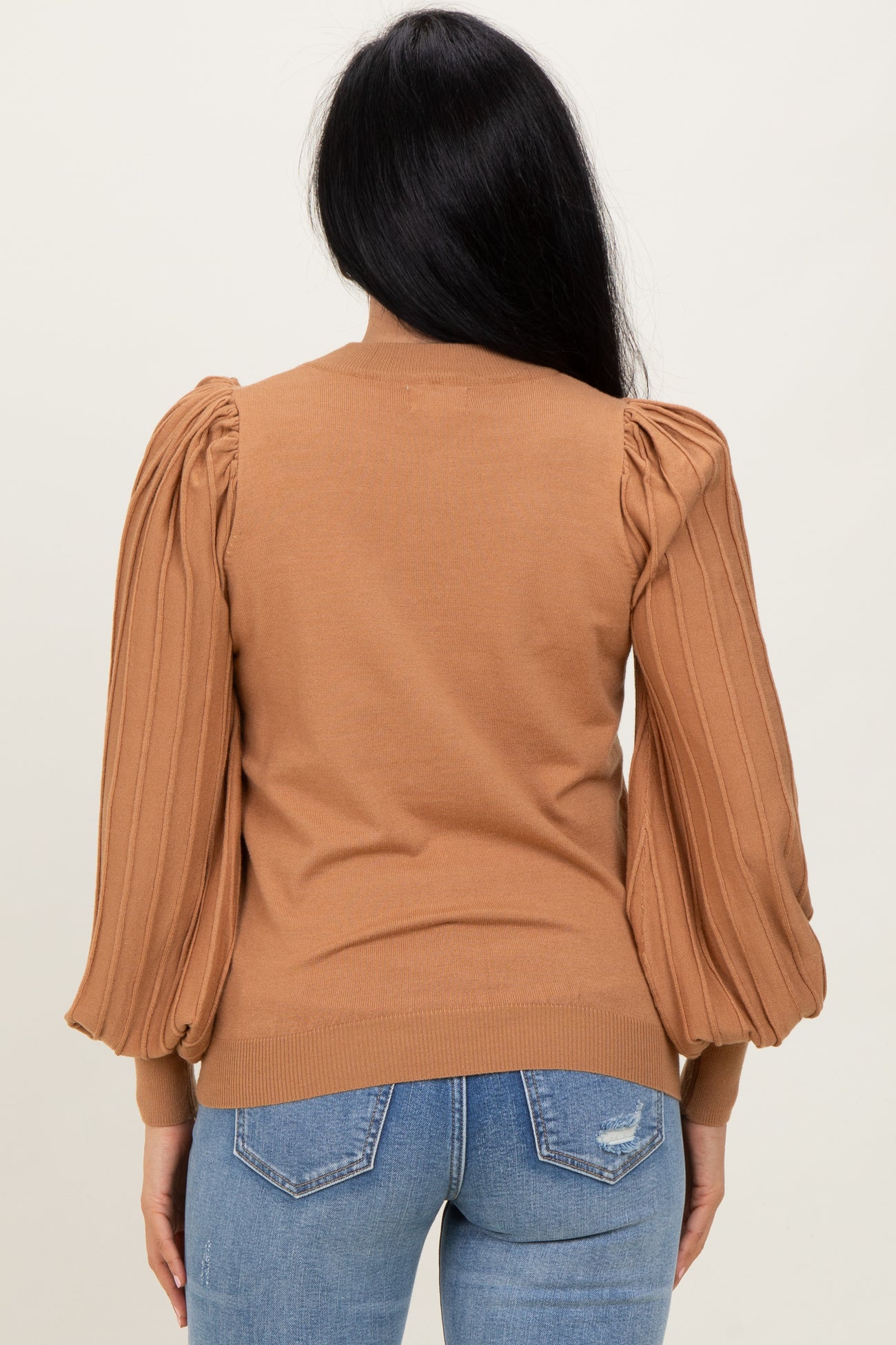 woman wearing a camel brown sweater with balloon sleeves, viewed from the back with blue jeans