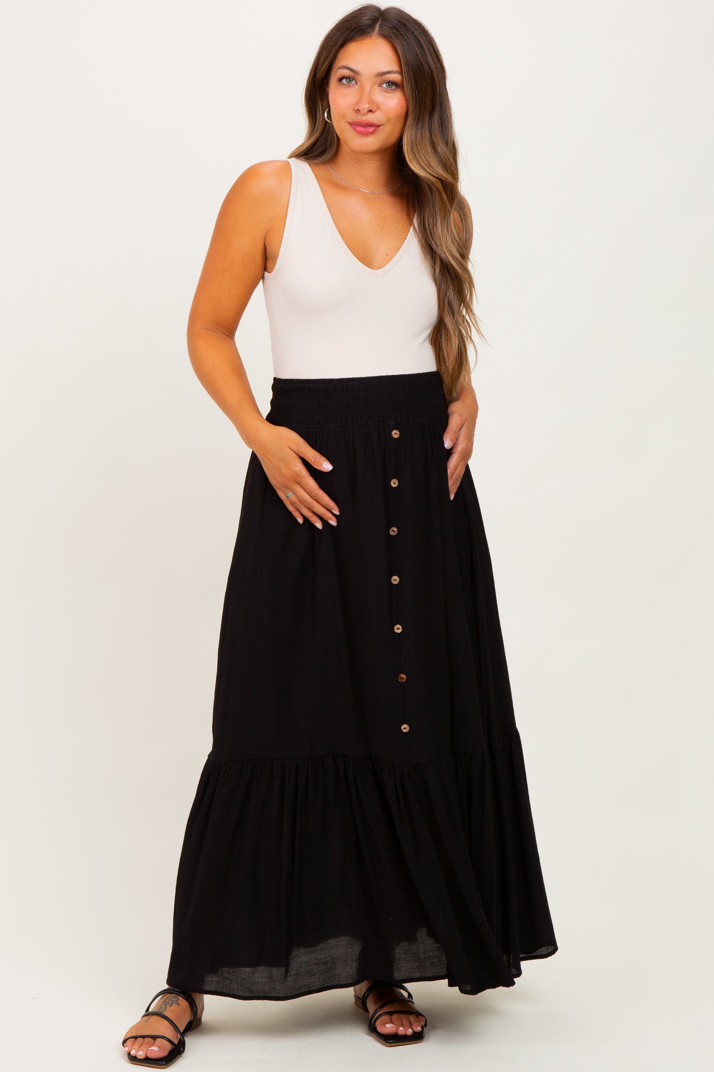 woman wearing a white maternity bodysuit and a black tiered maxi skirt with buttons, highlighting her baby bump