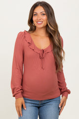 woman wearing a rust ribbed maternity top with ruffle details and a tie at the neckline, showcasing her baby bump
