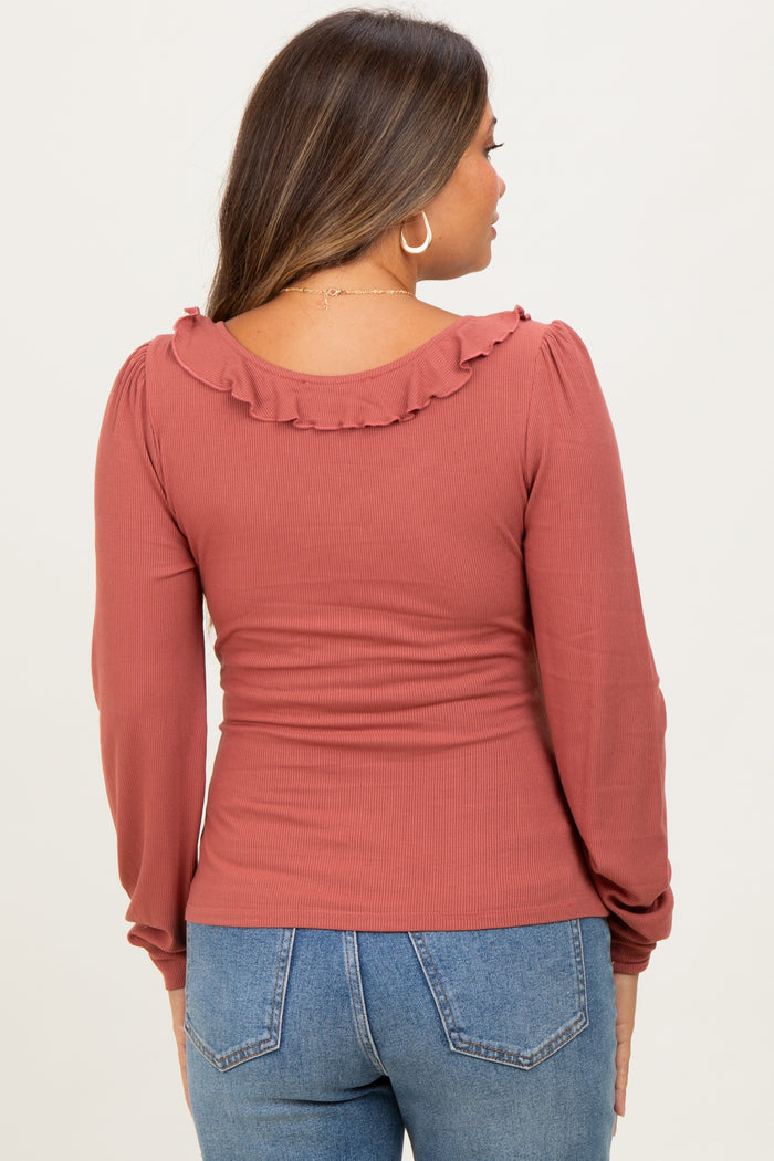 woman wearing a rust colored maternity top with ruffle detail on the neckline and long sleeves, showing a baby bump