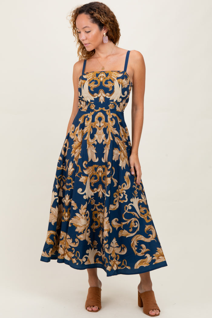 woman wearing a navy blue floral midi dress with spaghetti straps and a fitted bodice, styled with heeled sandals