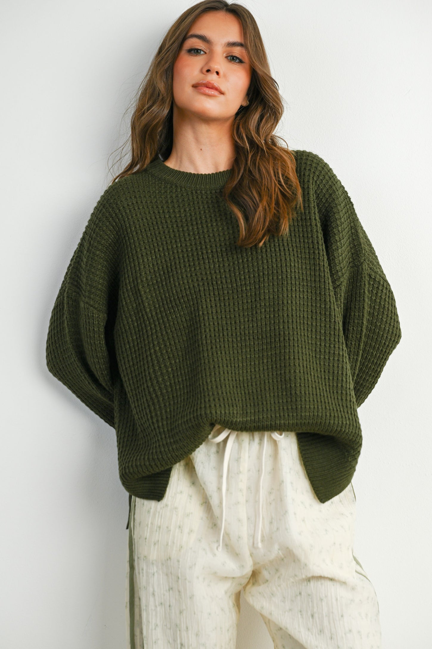 woman wearing a dark green knit sweater with a relaxed fit and long sleeves, paired with light patterned pants