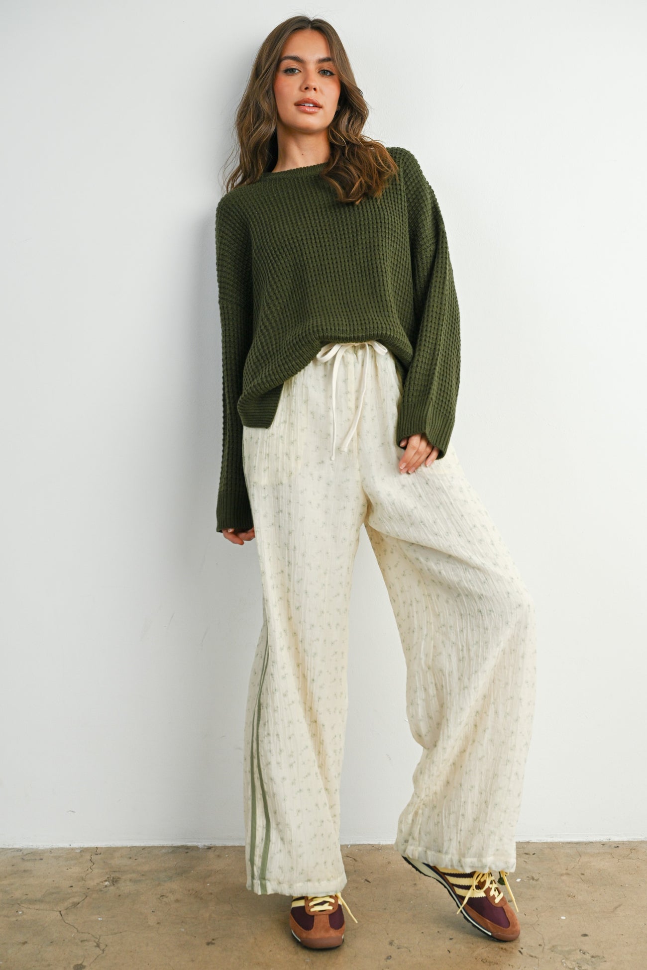 woman wearing an olive green oversized sweater and cream wide-leg pants with a subtle pattern and drawstring waist