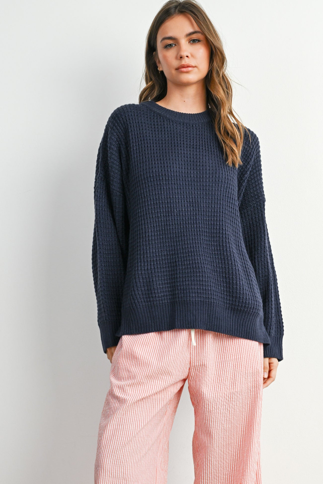woman wearing a navy blue waffle knit oversized sweater and pink striped wide-leg pants