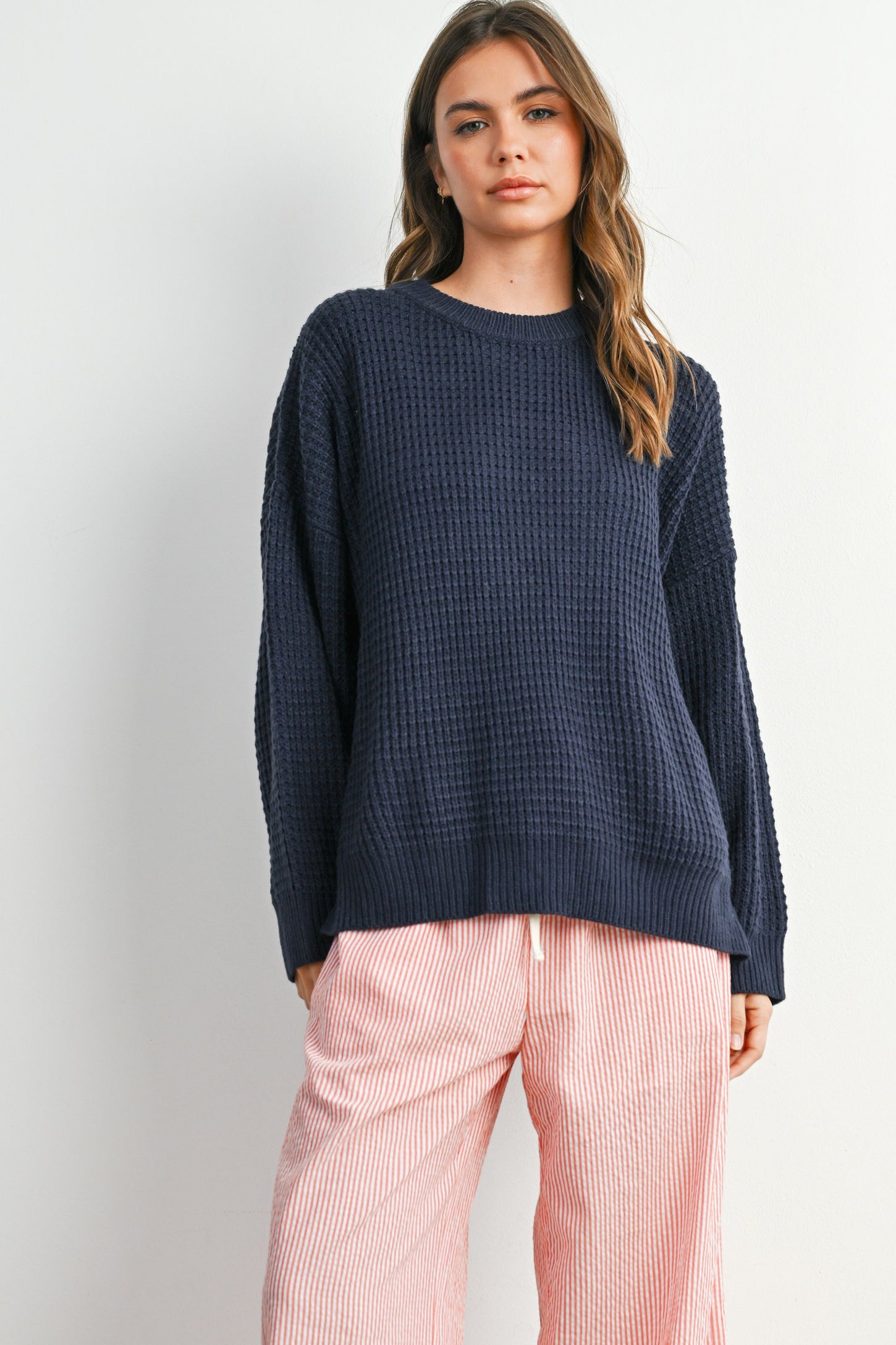 woman wearing a navy blue waffle knit oversized sweater and pink striped wide-leg pants