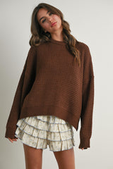 woman wearing a brown oversized waffle knit sweater and a cream ruffled floral mini skirt