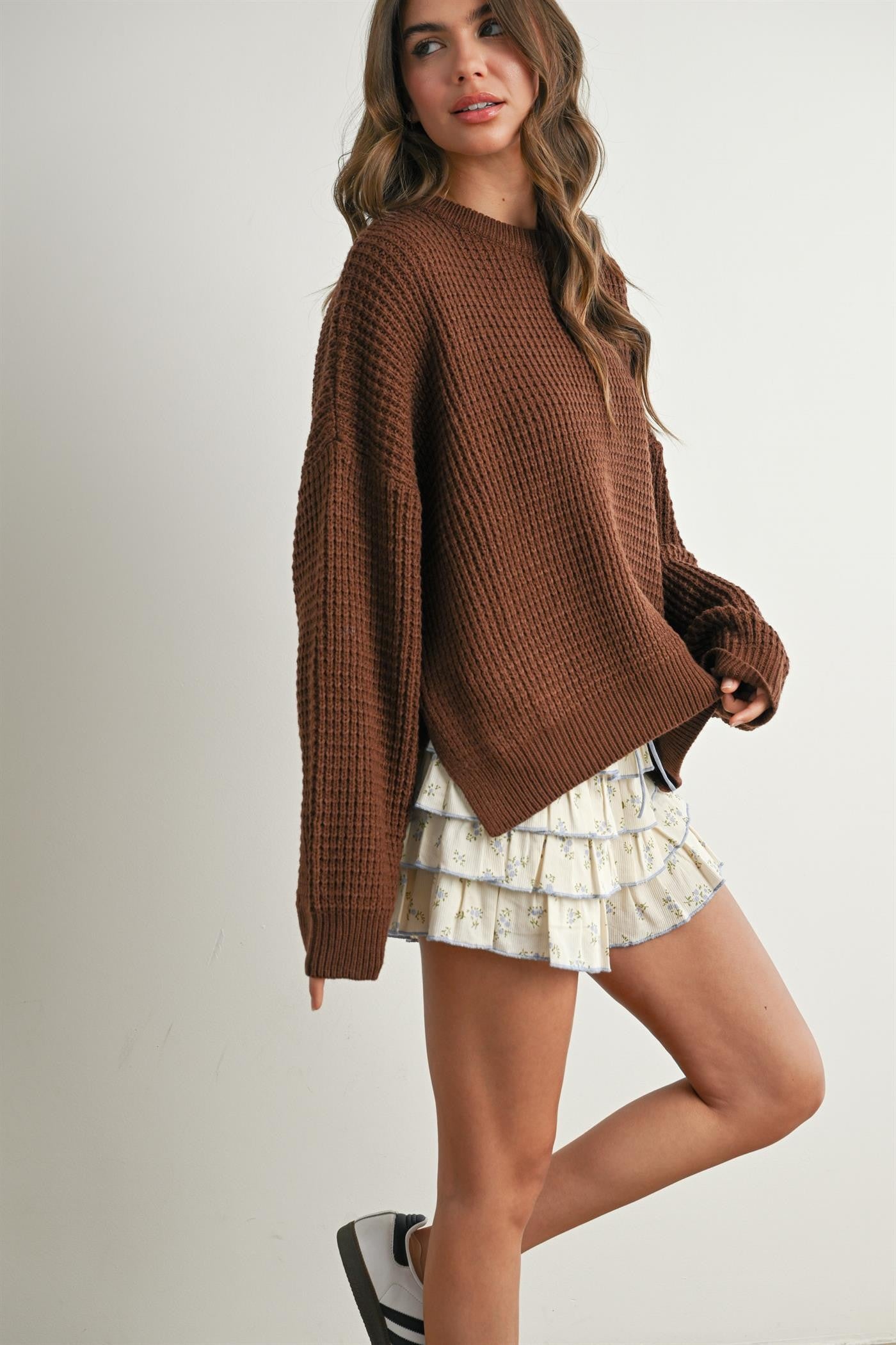 woman wearing a brown oversized waffle knit sweater paired with a white ruffled mini skirt and casual shoes