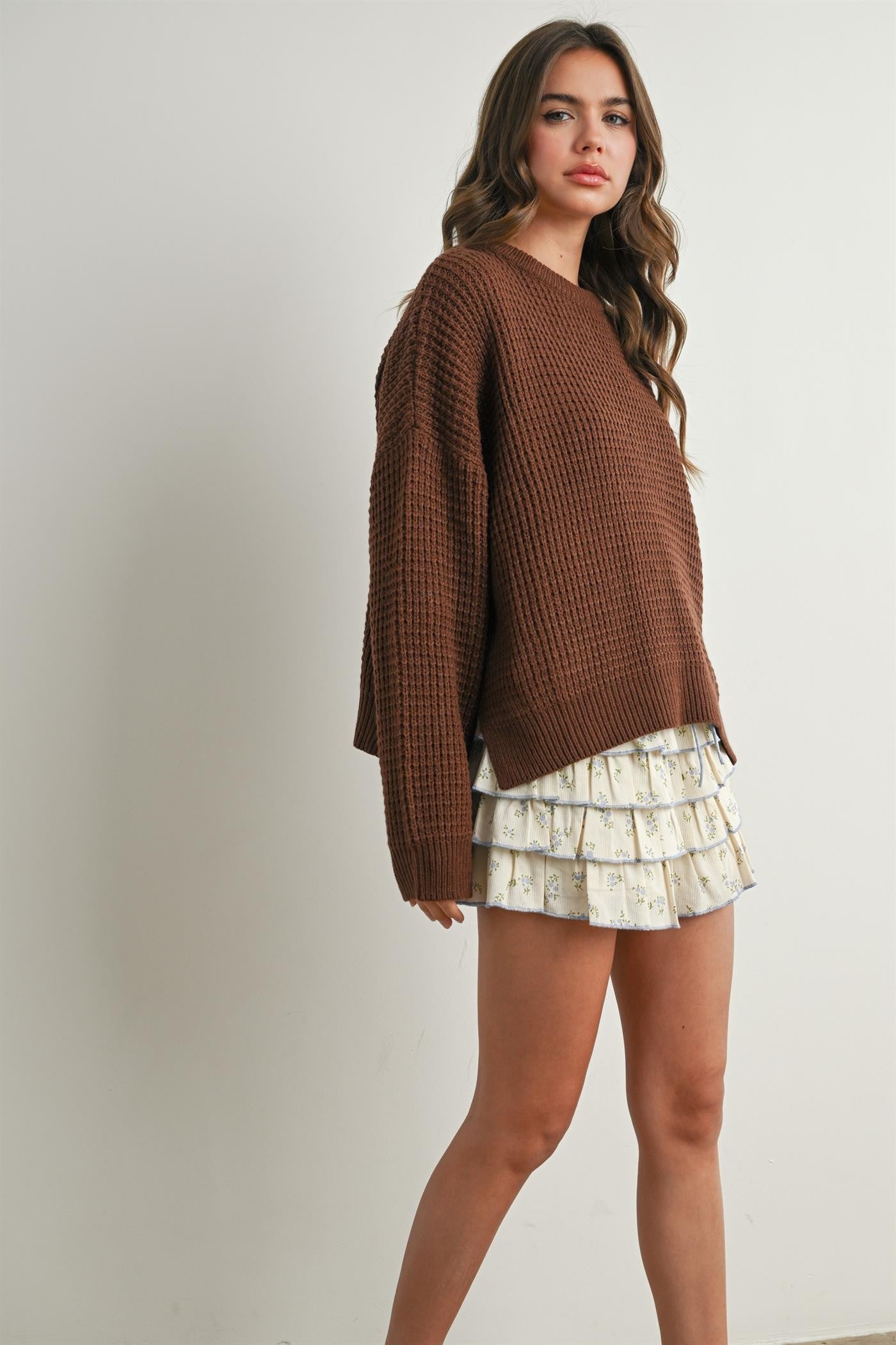 woman wearing a brown knitted sweater paired with a white ruffled mini skirt