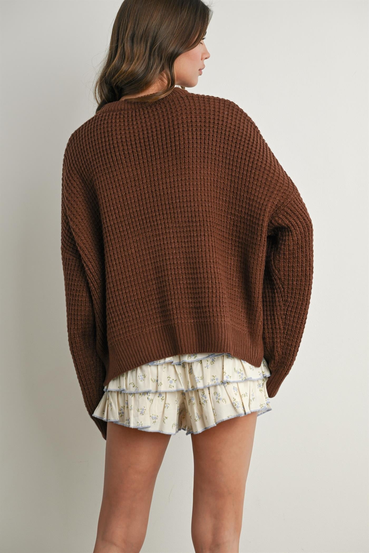 woman wearing a loose-fitting brown waffle knit sweater with a ruffled cream floral mini skirt