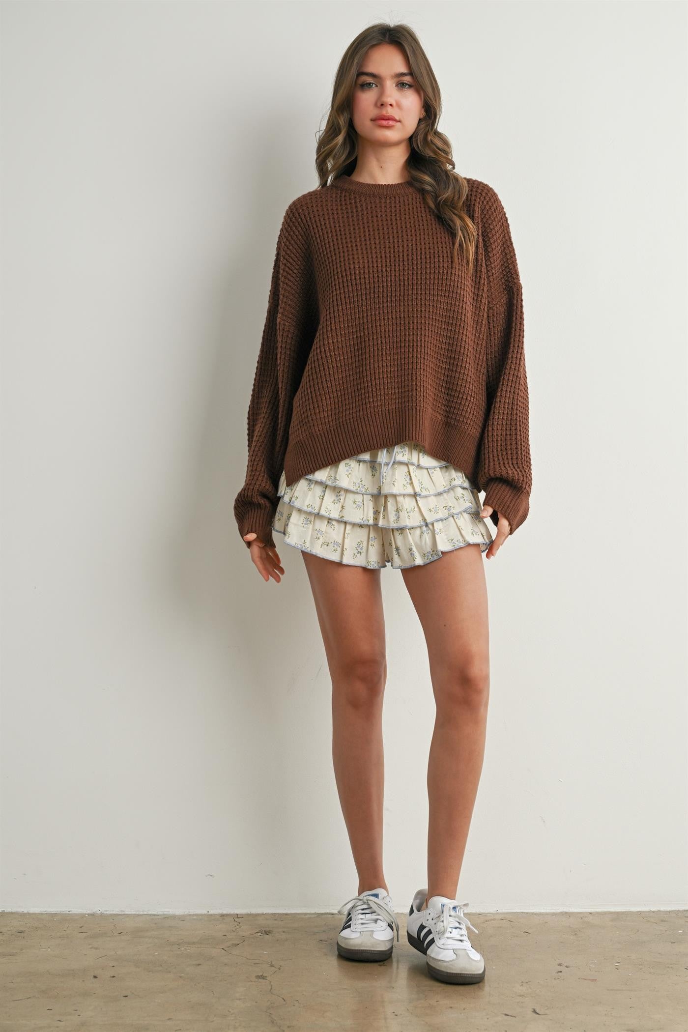 woman wearing an oversized brown knit sweater and cream floral ruffled shorts with sneakers