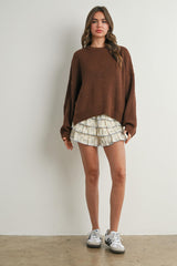 woman wearing an oversized brown knit sweater and cream floral ruffled shorts with sneakers