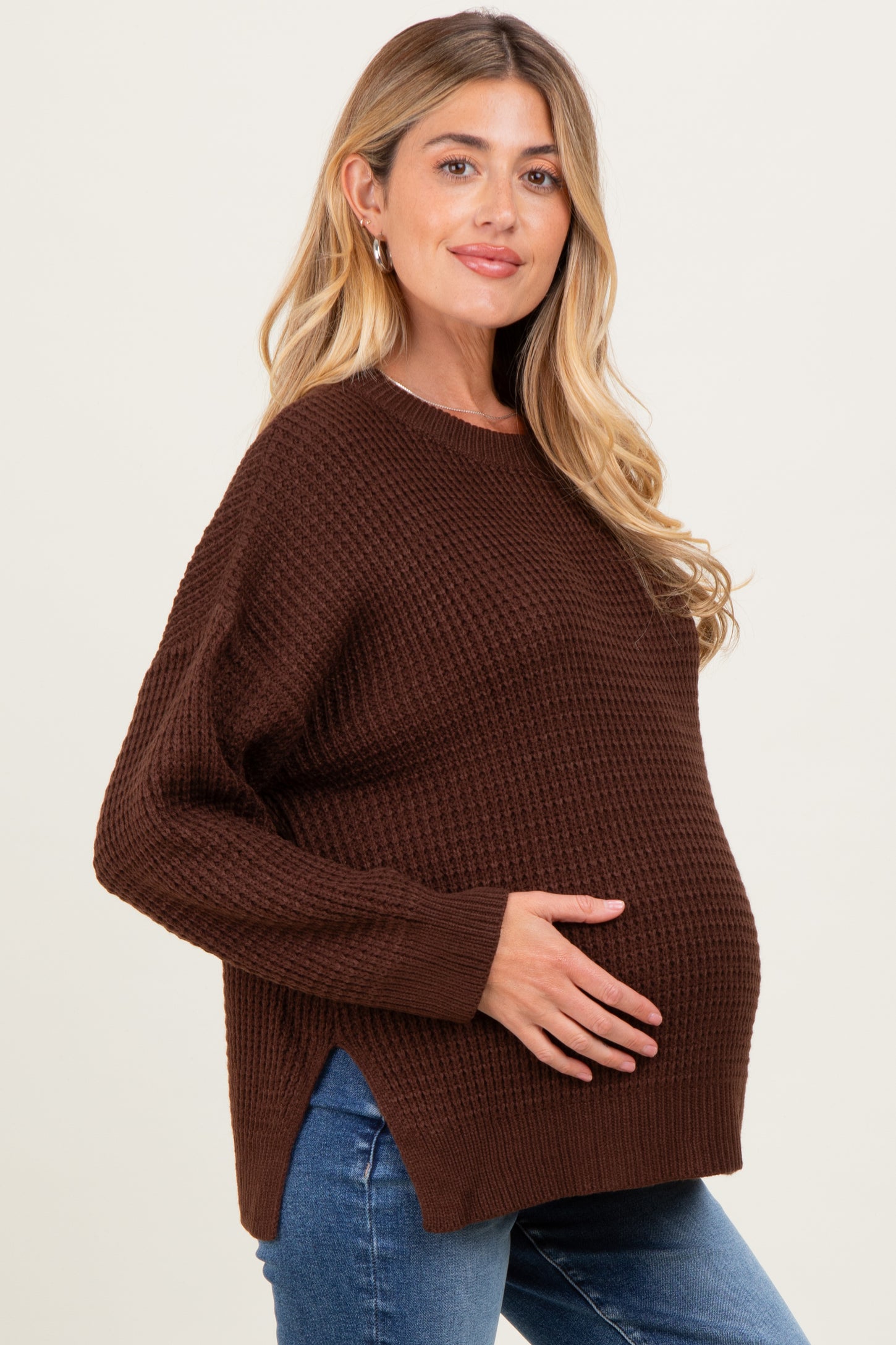woman wearing a brown maternity sweater with side slits and a visible baby bump