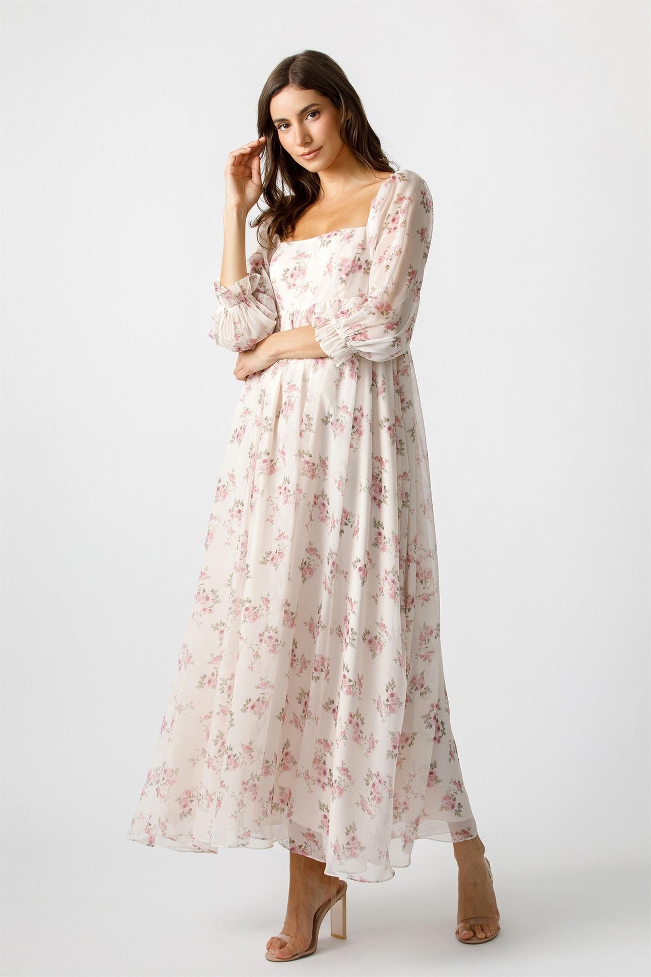 woman wearing a long sleeve floral maxi dress with a square neckline and flowy skirt standing against a plain background