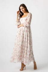 woman wearing a long sleeve floral maxi dress with a square neckline and flowy skirt standing against a plain background