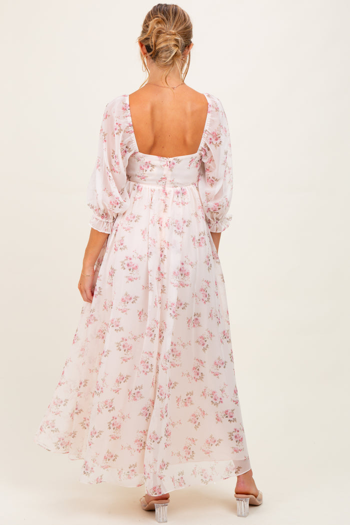 woman wearing a floral maternity maxi dress with puff sleeves and a low back, showing a baby bump