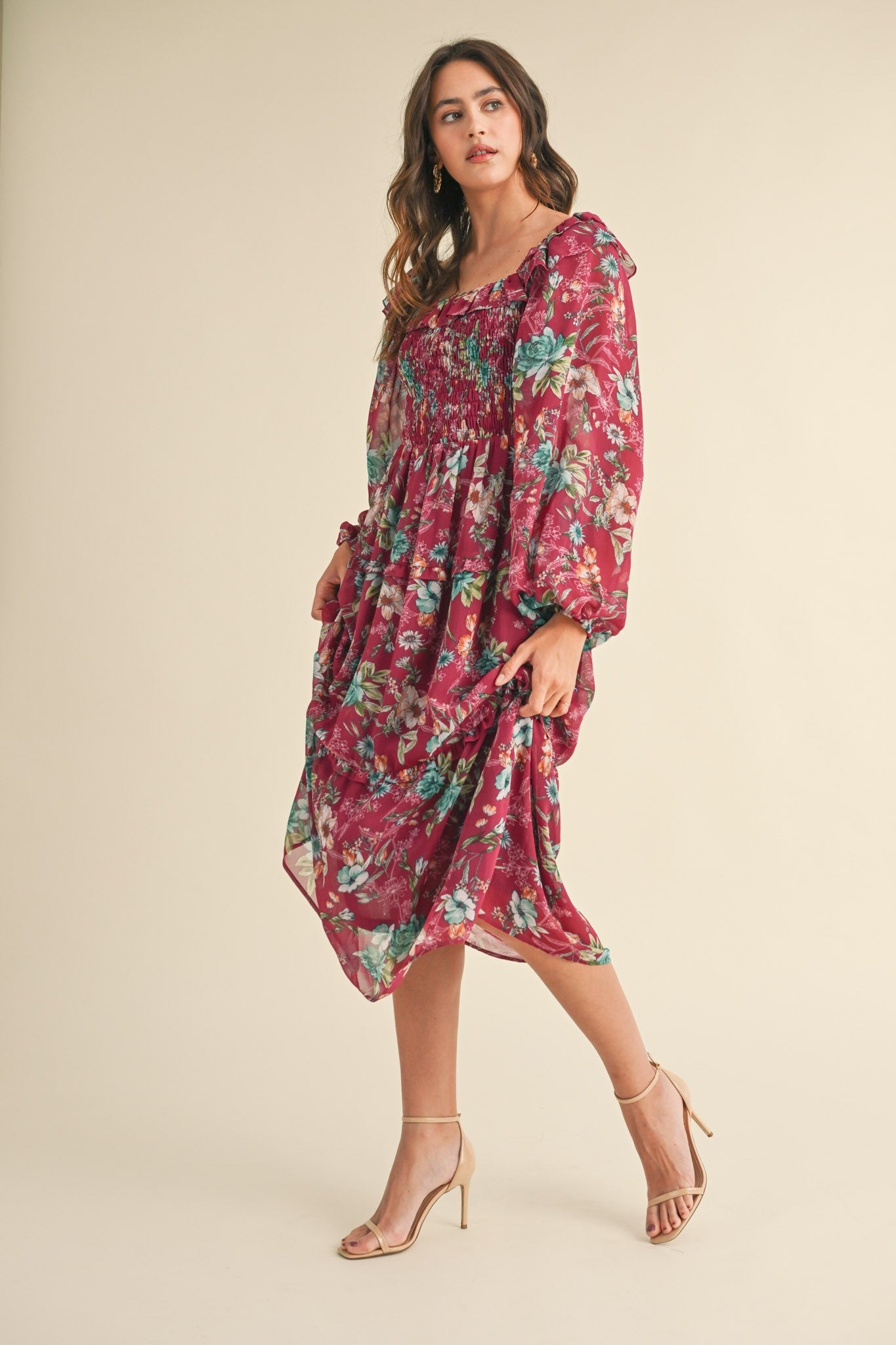 woman wearing a burgundy floral midi dress with smocked bodice and long sleeves, standing in a relaxed pose