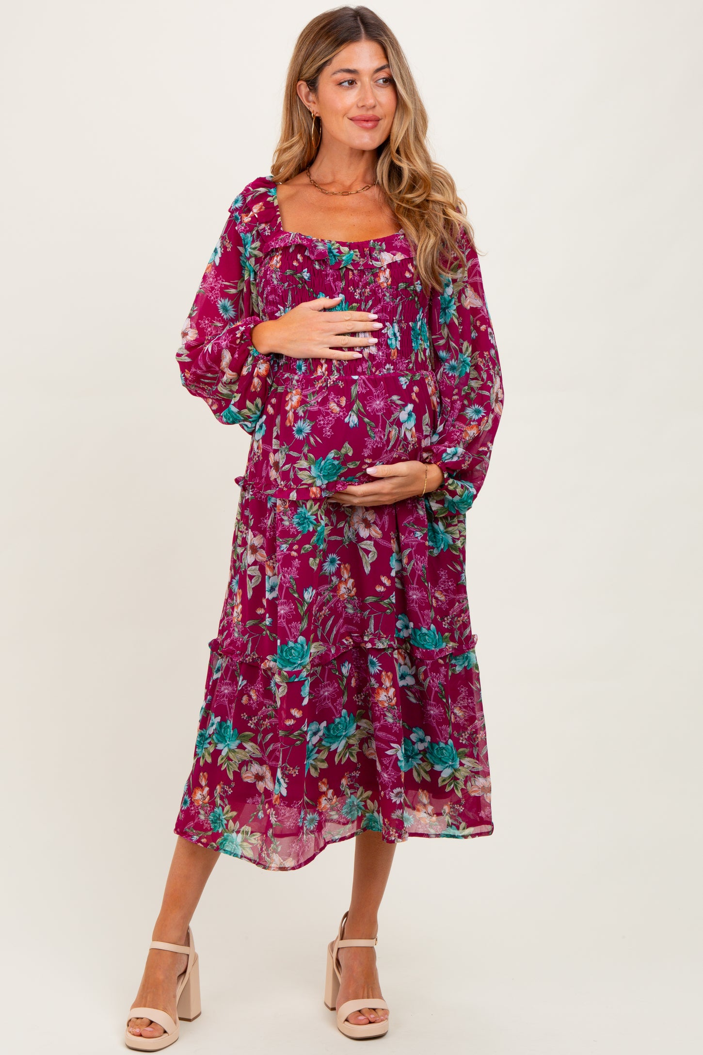 woman wearing a purple floral maternity dress with a tiered design and holding her baby bump