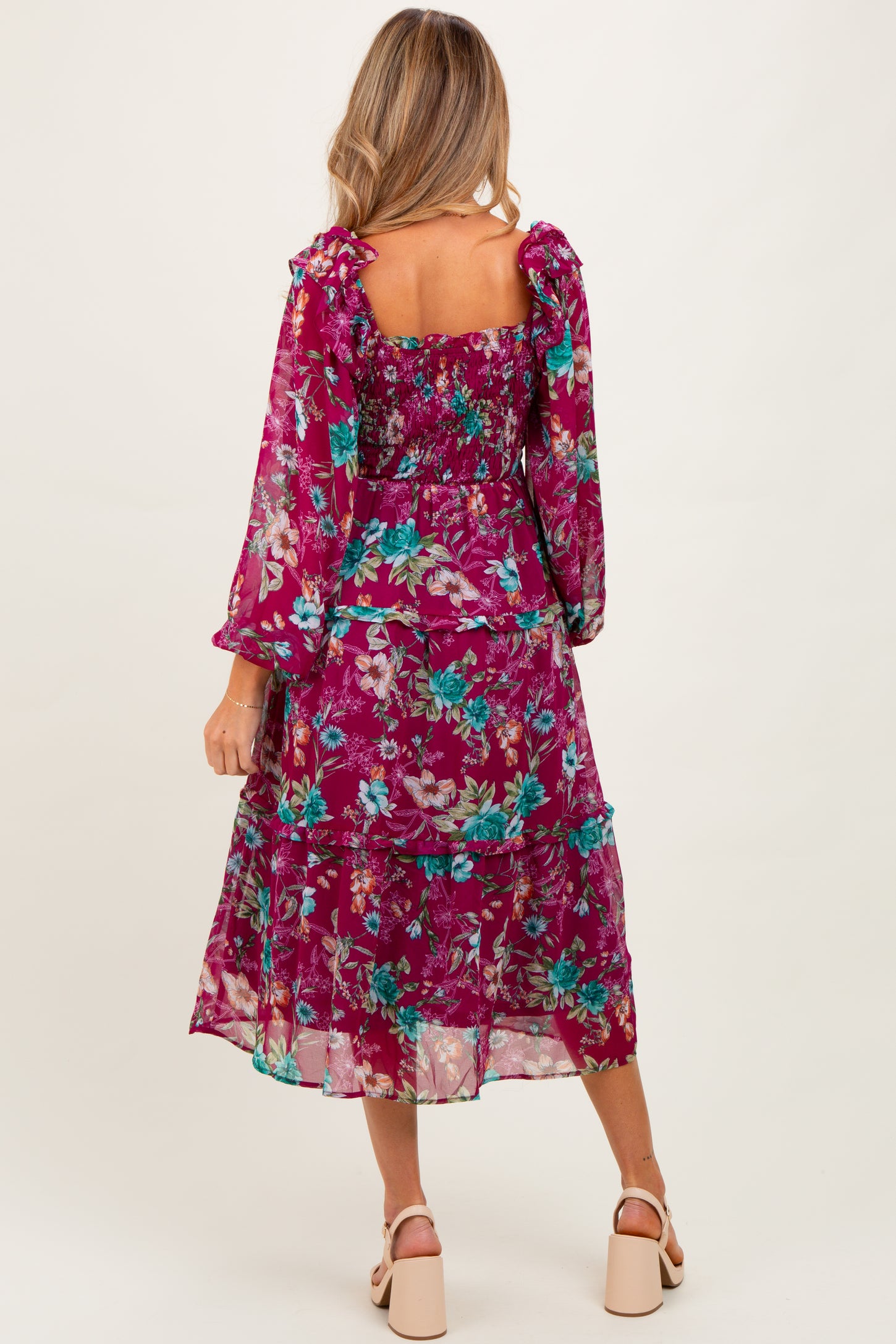 woman wearing a floral purple maternity dress with tiered layers and long sleeves, showing her back