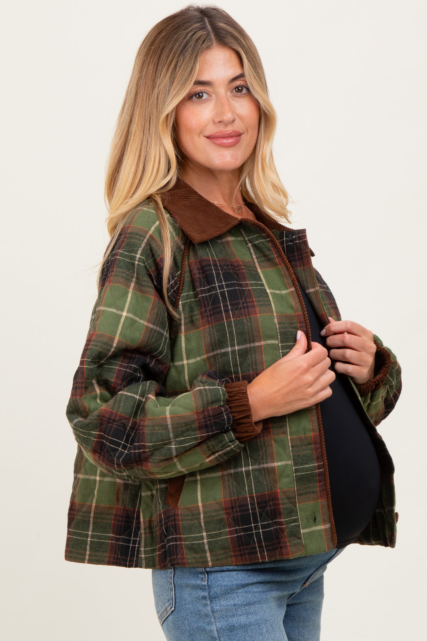woman wearing a green and brown plaid maternity jacket with a brown collar and elastic cuffs, and showcasing her baby bump