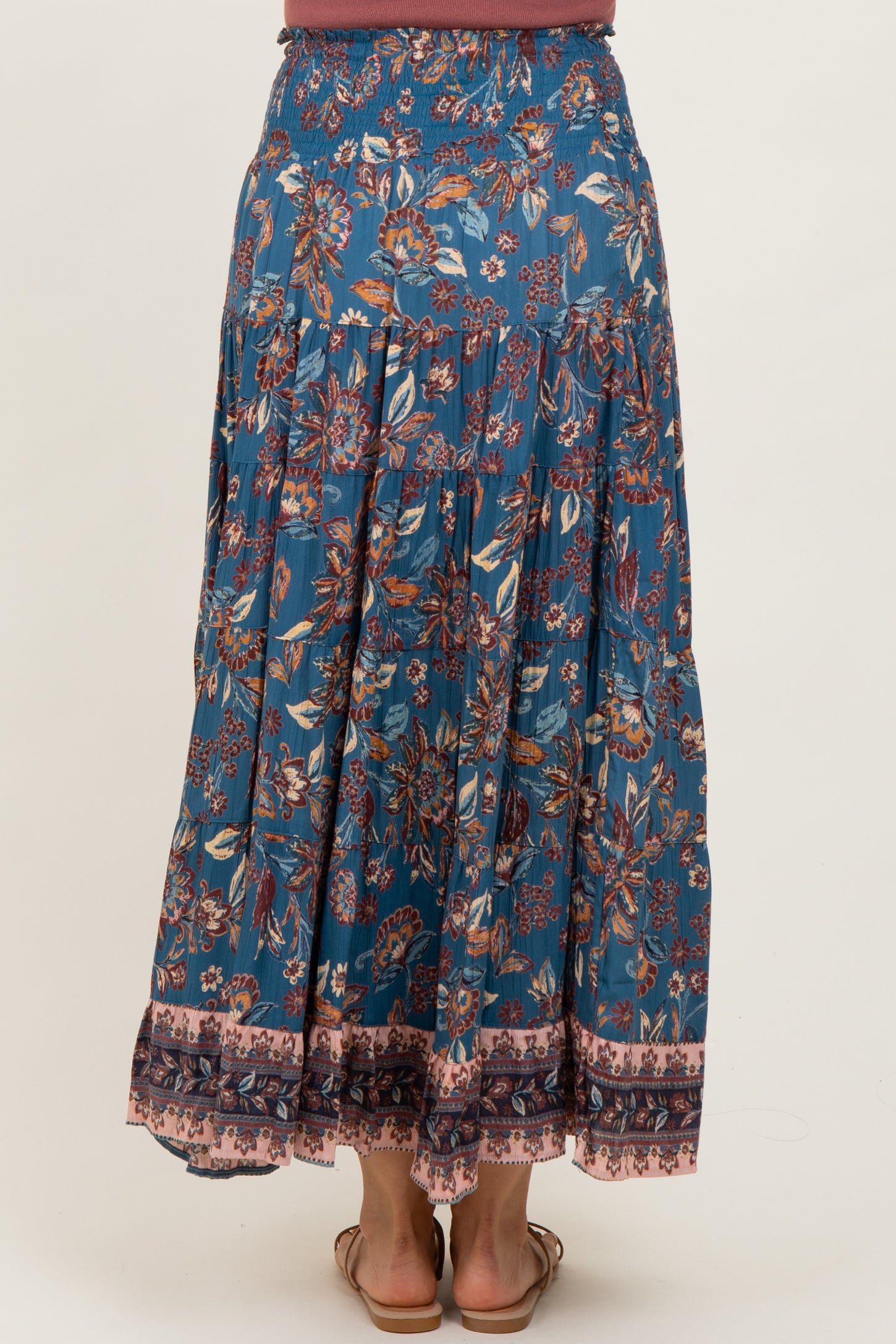 woman wearing a flowy blue floral maxi skirt with an elastic waistband and tiered design, viewed from the back