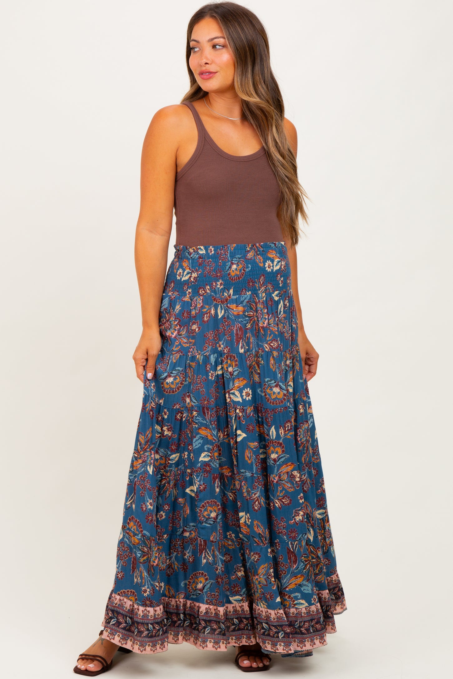 woman wearing a brown tank top and a blue floral maternity maxi skirt with a flowing bottom and a decorative hem