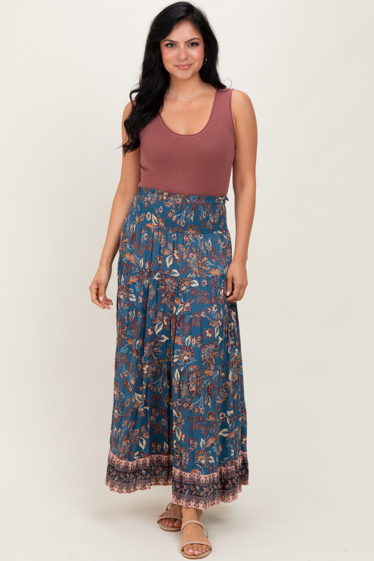 woman wearing a rust sleeveless top with a blue floral maxi skirt and sandals