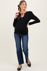 woman wearing a black ribbed maternity top with a brown tie detail at the neckline and blue jeans, showing her baby bump
