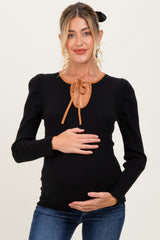 woman wearing a black ribbed maternity top with puff sleeves and a brown tie detail, holding her baby bump