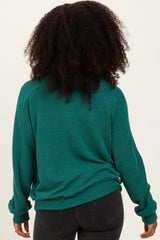 woman wearing a teal ribbed long sleeve sweater, viewed from the back, paired with black jeans