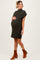 woman wearing a dark green ribbed maternity dress with short sleeves and a pocket, cradling her baby bump