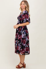 woman wearing a black floral midi dress with puff sleeves and a smocked waist, standing in profile