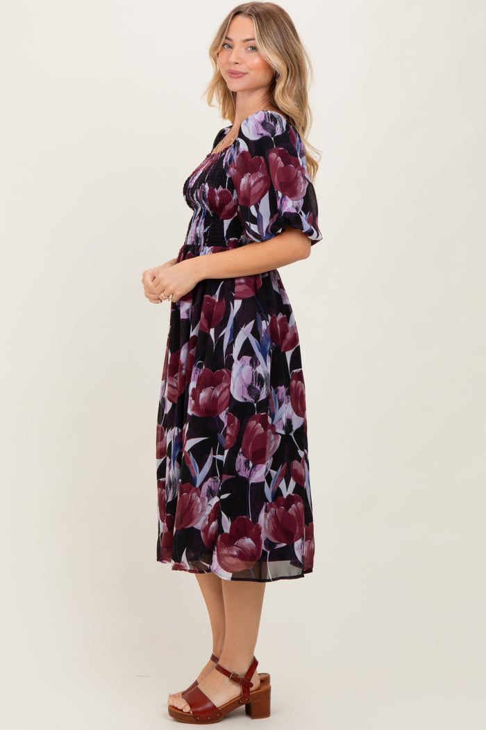woman wearing a black floral midi dress with puff sleeves and a smocked waist, standing in profile