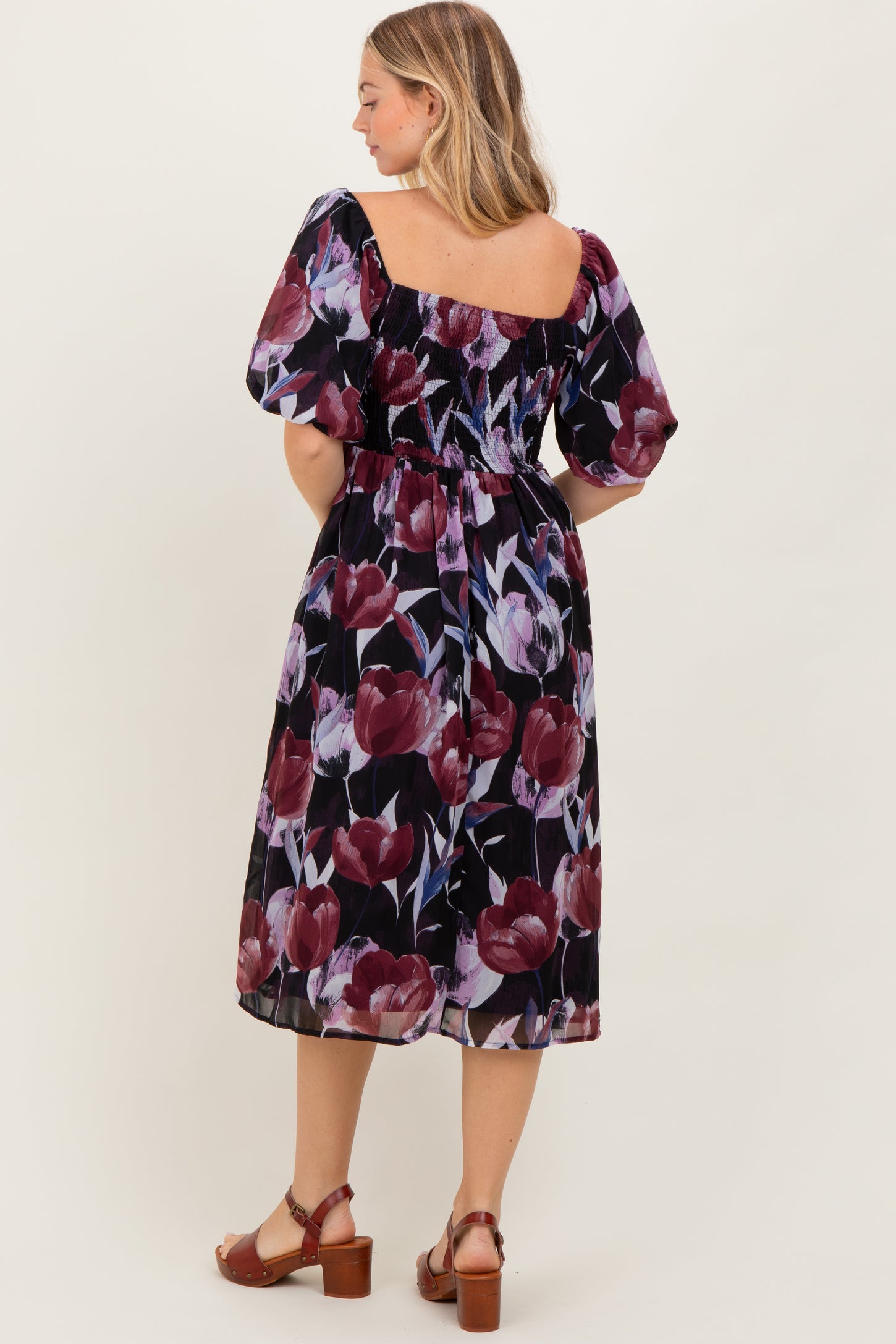 woman wearing a black floral mid-length dress with puff sleeves and a gathered waist, viewed from the back