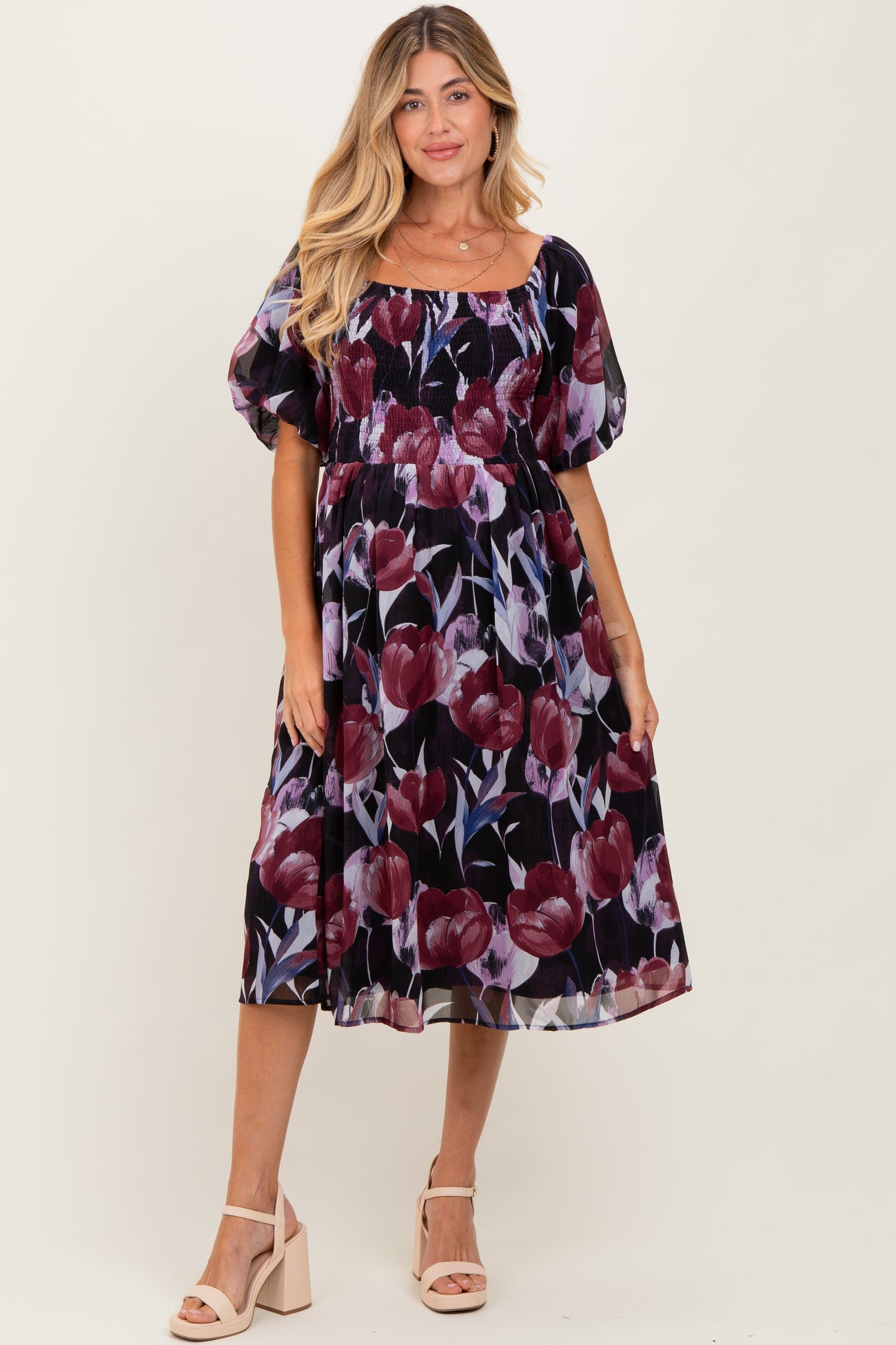 woman wearing a floral maternity dress with a square neckline and puff sleeves, standing in a neutral background
