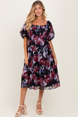 woman wearing a floral maternity dress with a square neckline and puff sleeves, standing in a neutral background
