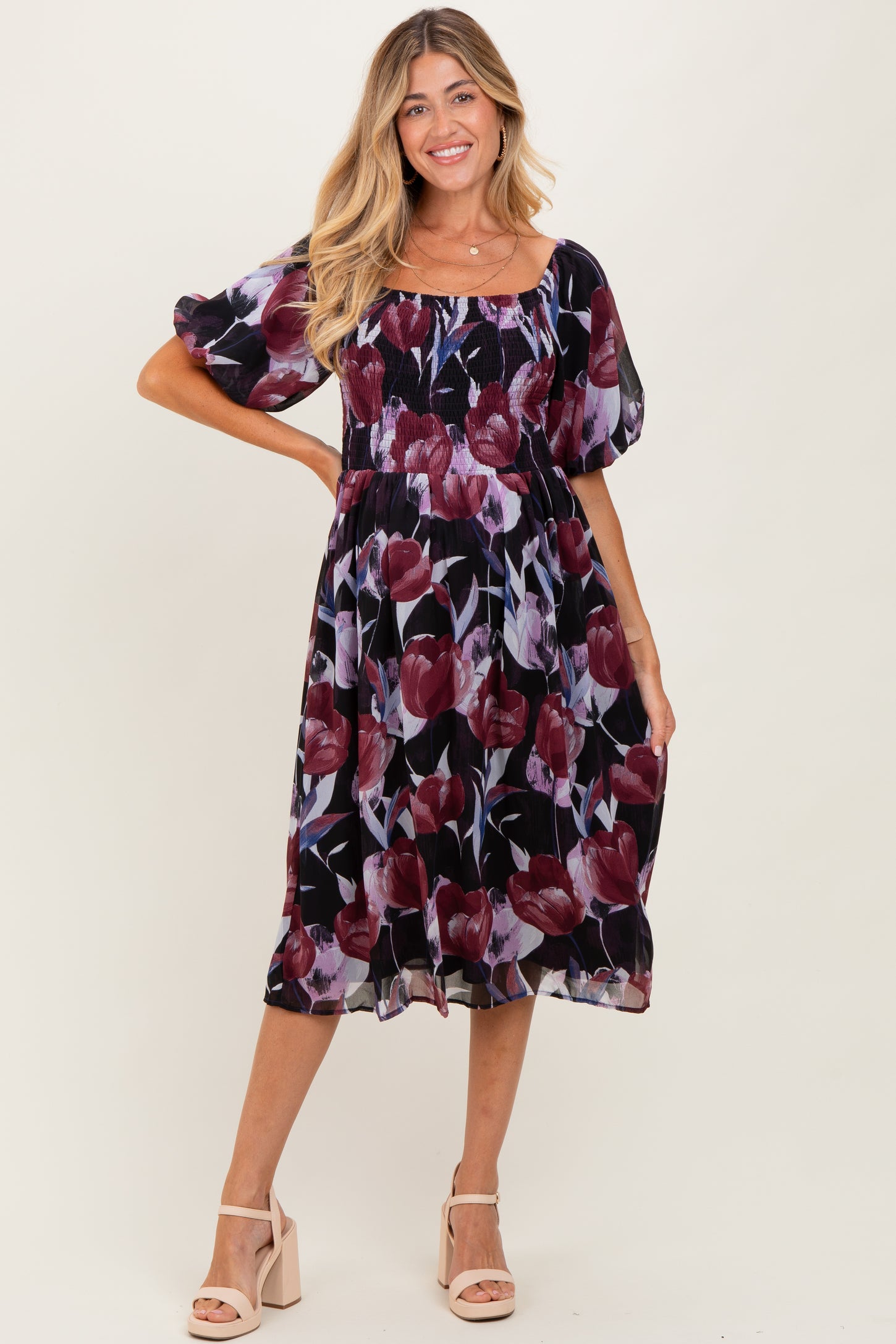 woman wearing a floral maternity dress with puff sleeves and a fitted bodice, posing and smiling