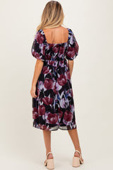 woman wearing a floral black and purple maternity dress with puff sleeves and a smocked bodice, showing her baby bump