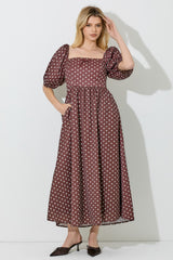 woman wearing a brown polka dot maxi dress with puff sleeves and pockets, standing against a white background