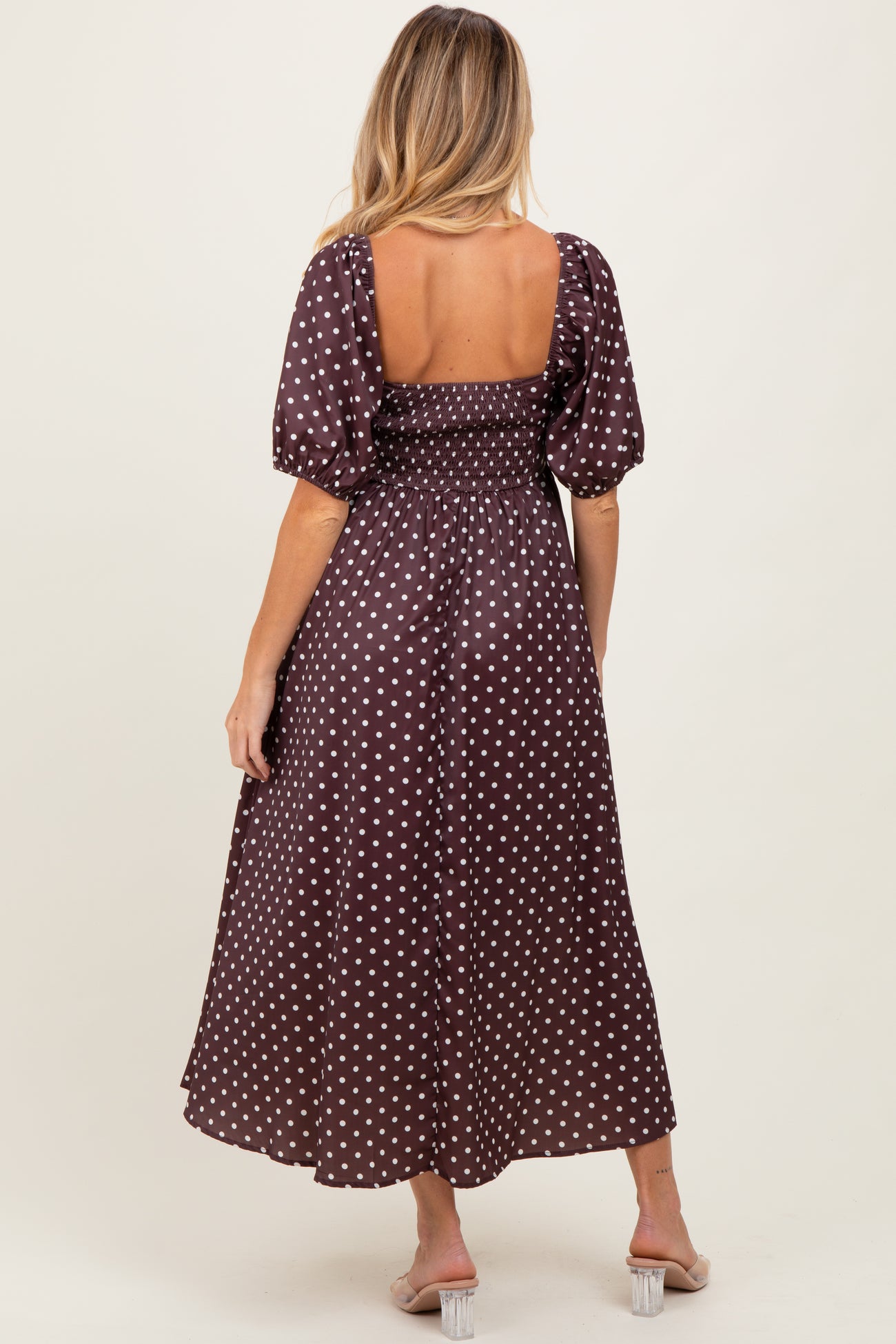 woman wearing a brown polka dot maternity dress with a smocked bodice and puff sleeves, showing a baby bump from behind