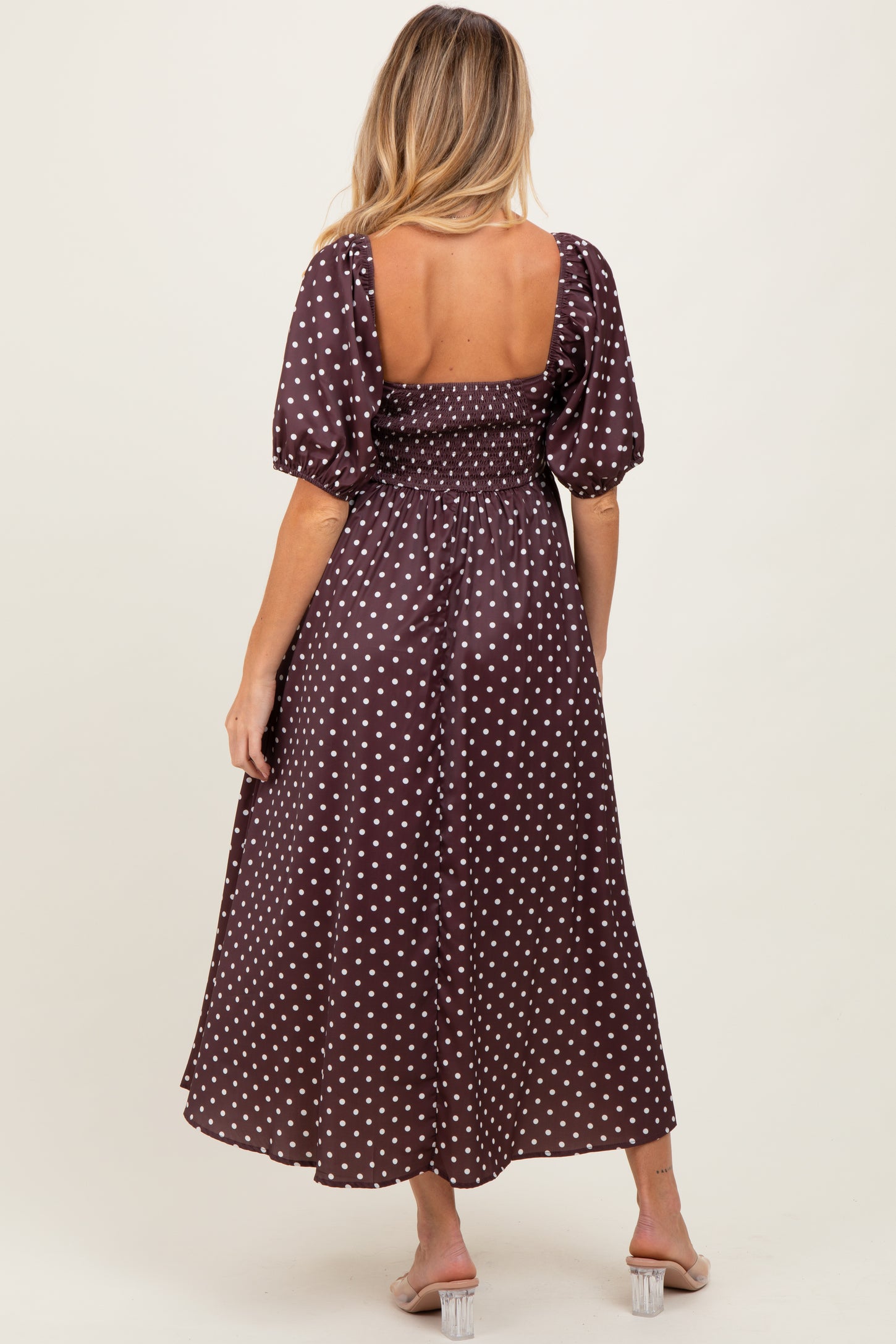woman wearing a brown polka dot maternity dress with a smocked bodice and puff sleeves, showing a baby bump from behind