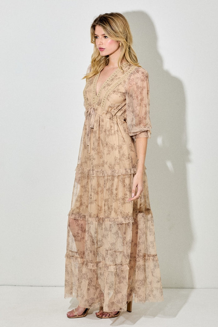woman wearing a beige floral maxi dress with a tie waist and sheer tiered layers