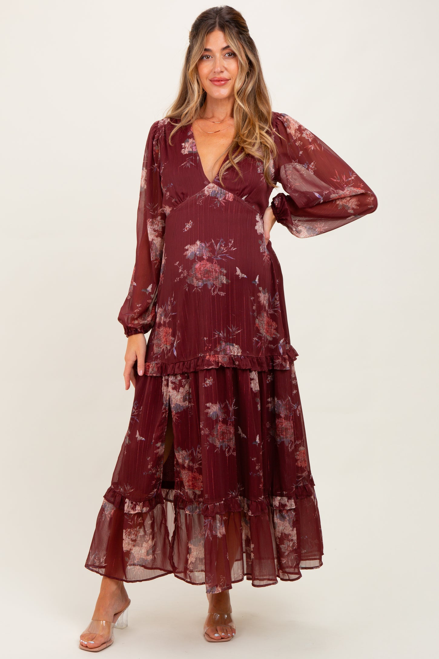 woman wearing a burgundy floral maternity dress with long sleeves and tiered ruffles, showing off her baby bump