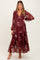 woman wearing a burgundy floral maternity dress with long sleeves and tiered ruffles, showing off her baby bump